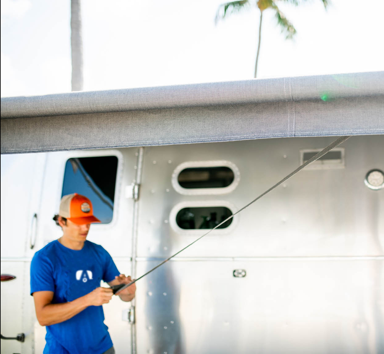 A man in a blue Airstream tshirt rolling out his Zip-Dee awning on his Airstream Travel Trailer
