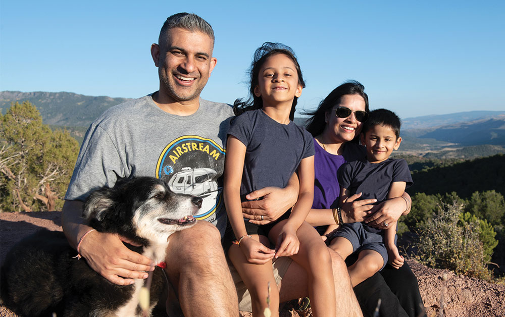 Family and dog sitting on a rock with mountains in the background
