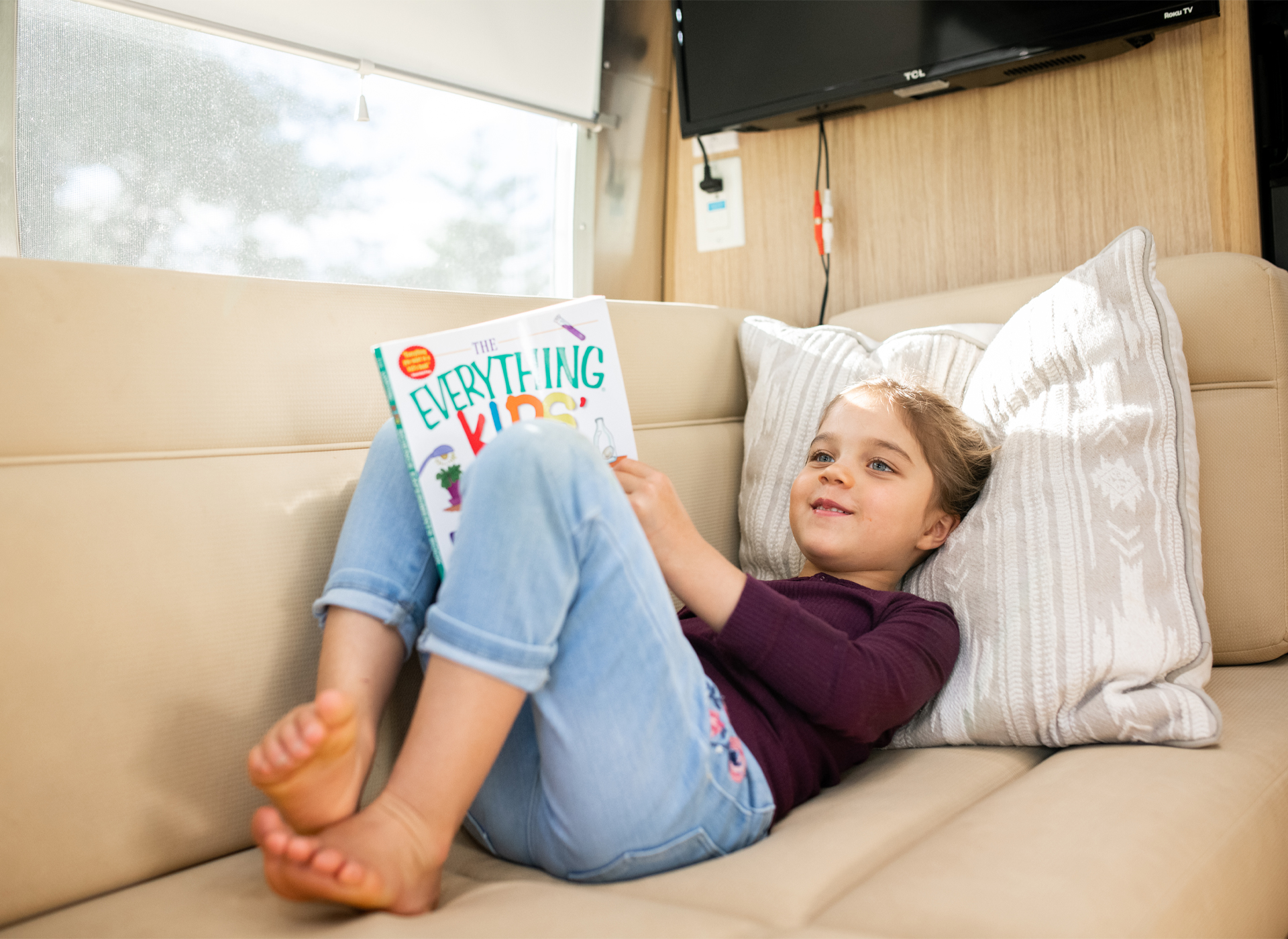 A girl laying on the couch in an Airstream reading a book
