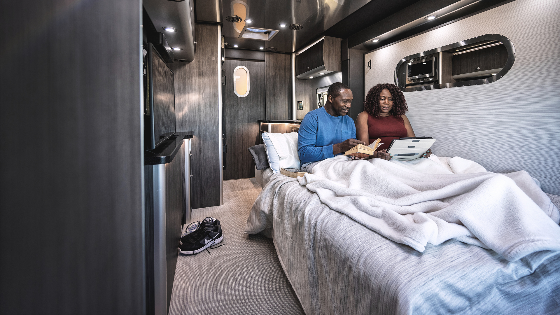 A couple sitting on the bed reading in their Airstream class B motorhome