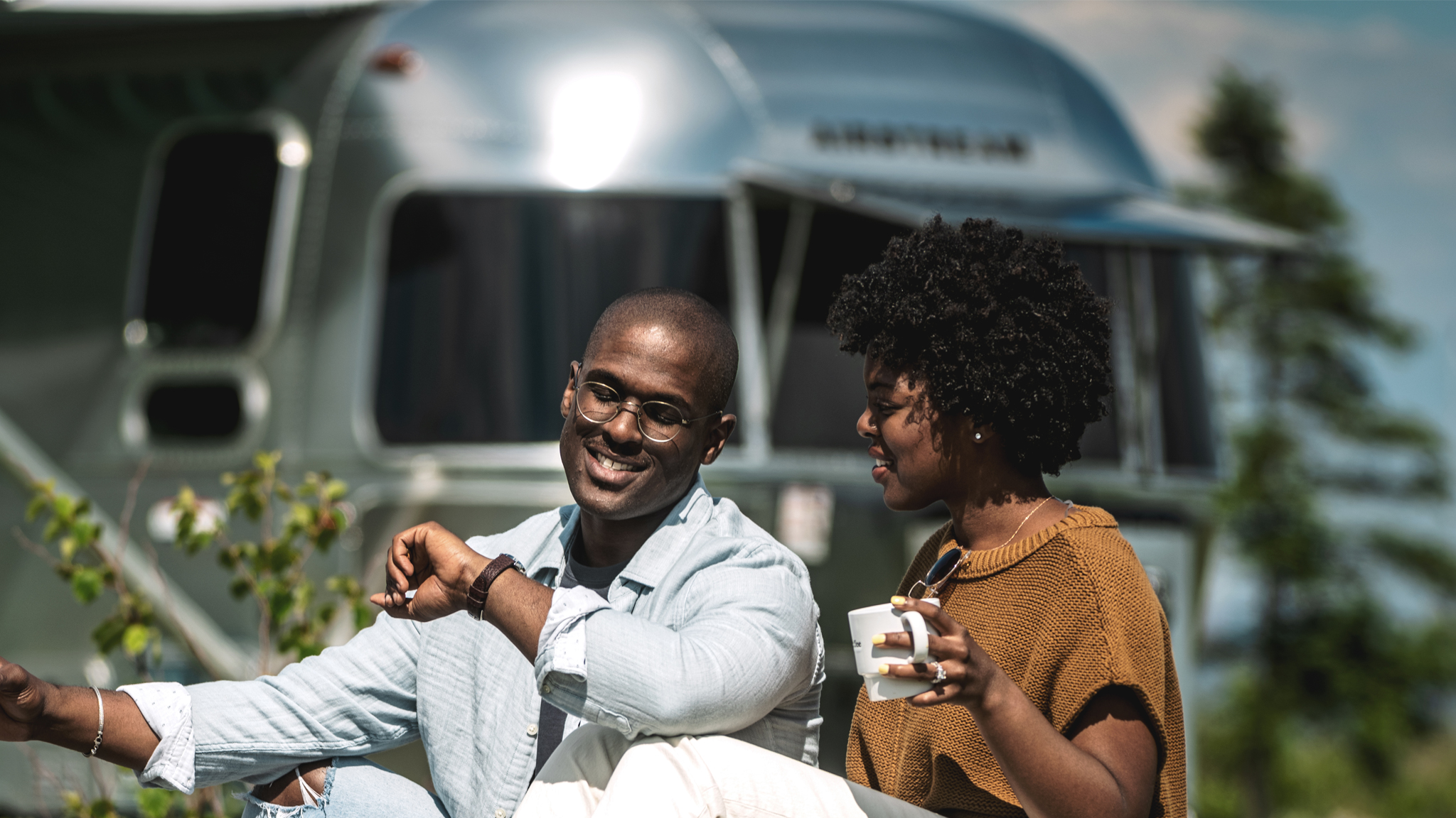 Two people drinking coffee outside of their airstream travel trailer