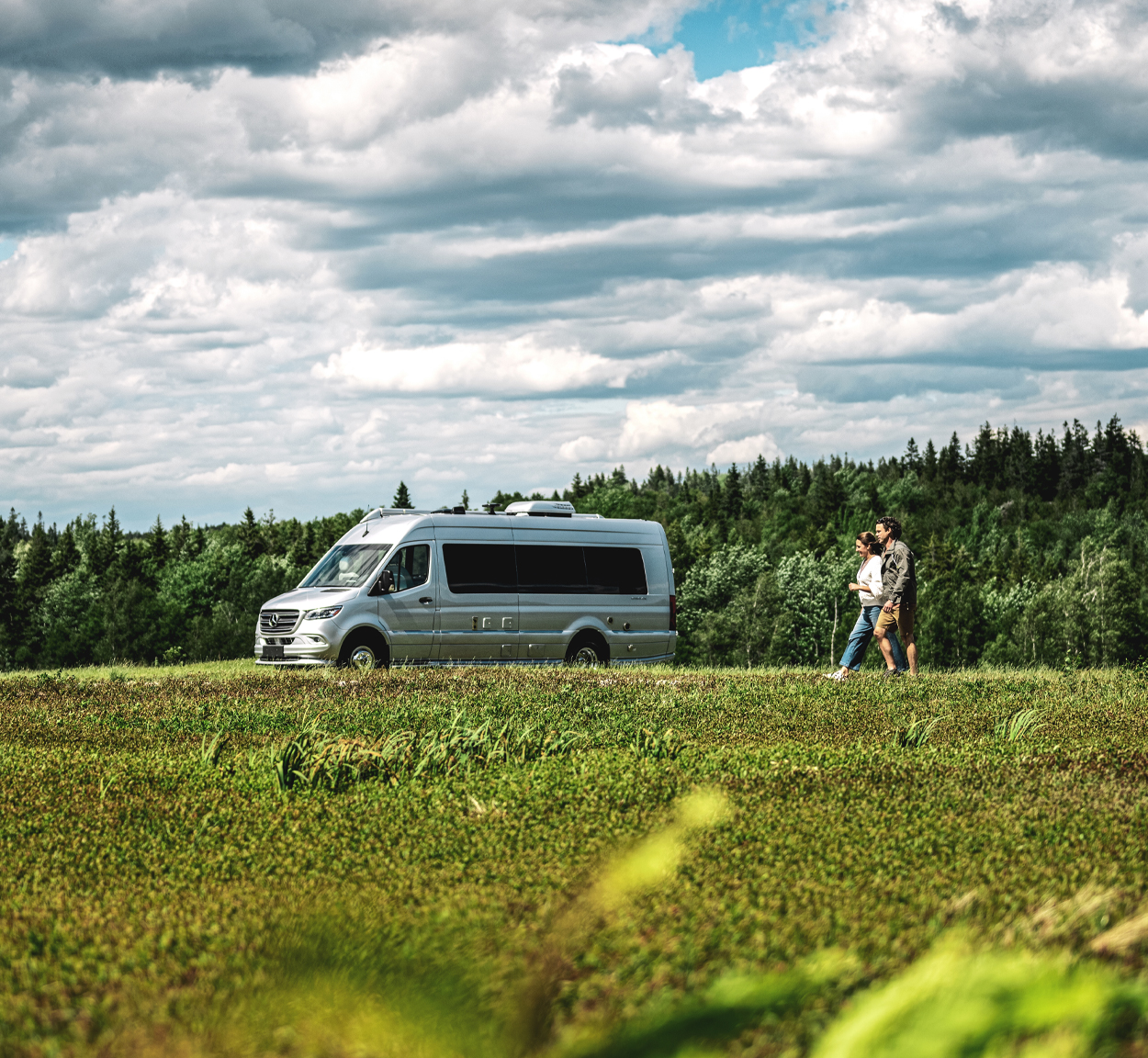 Airstream Interstate Touring Coach parked in a field with a couple walking outside.
