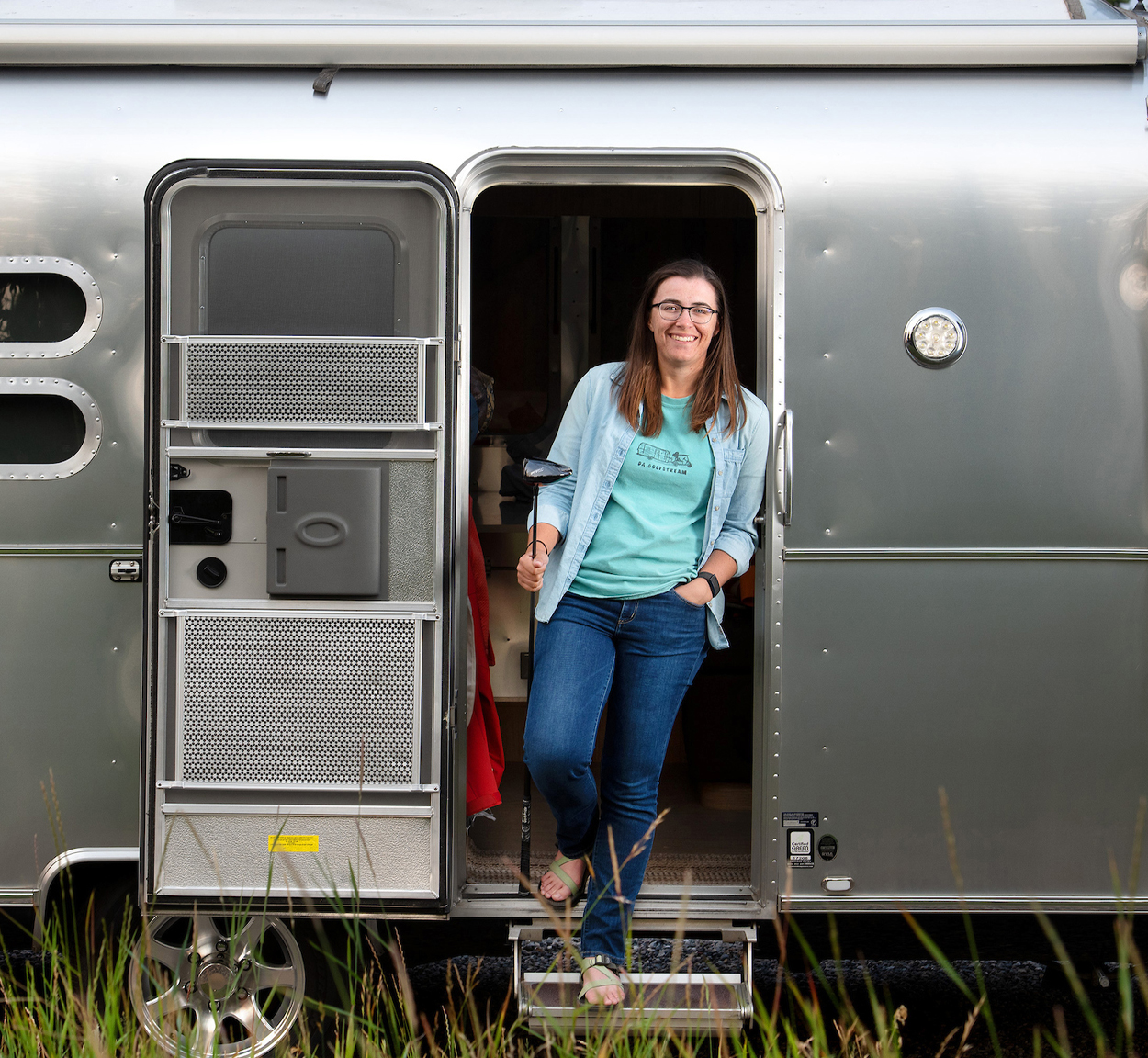 Dorsey Addicks inside the door of her Airstream Flying Cloud travel trailer holding a golf club.