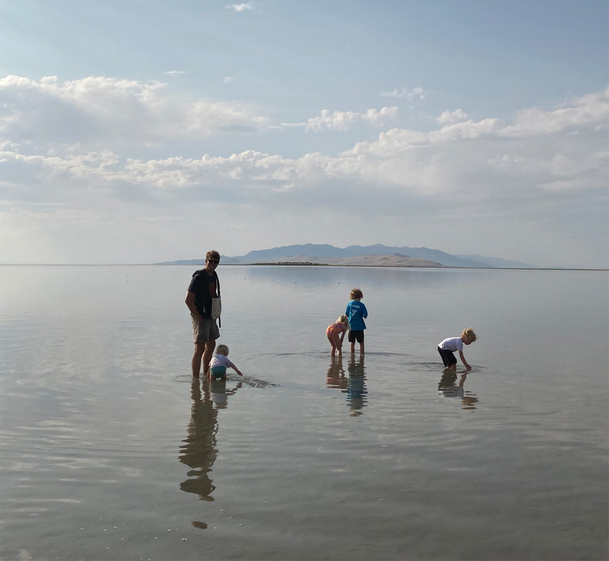 A family walking and playing in shallow water with a fog in the background.