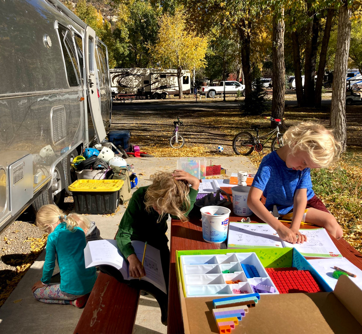 Kids sitting at a table outside of their Airstream travel trailer as they do school on the road.