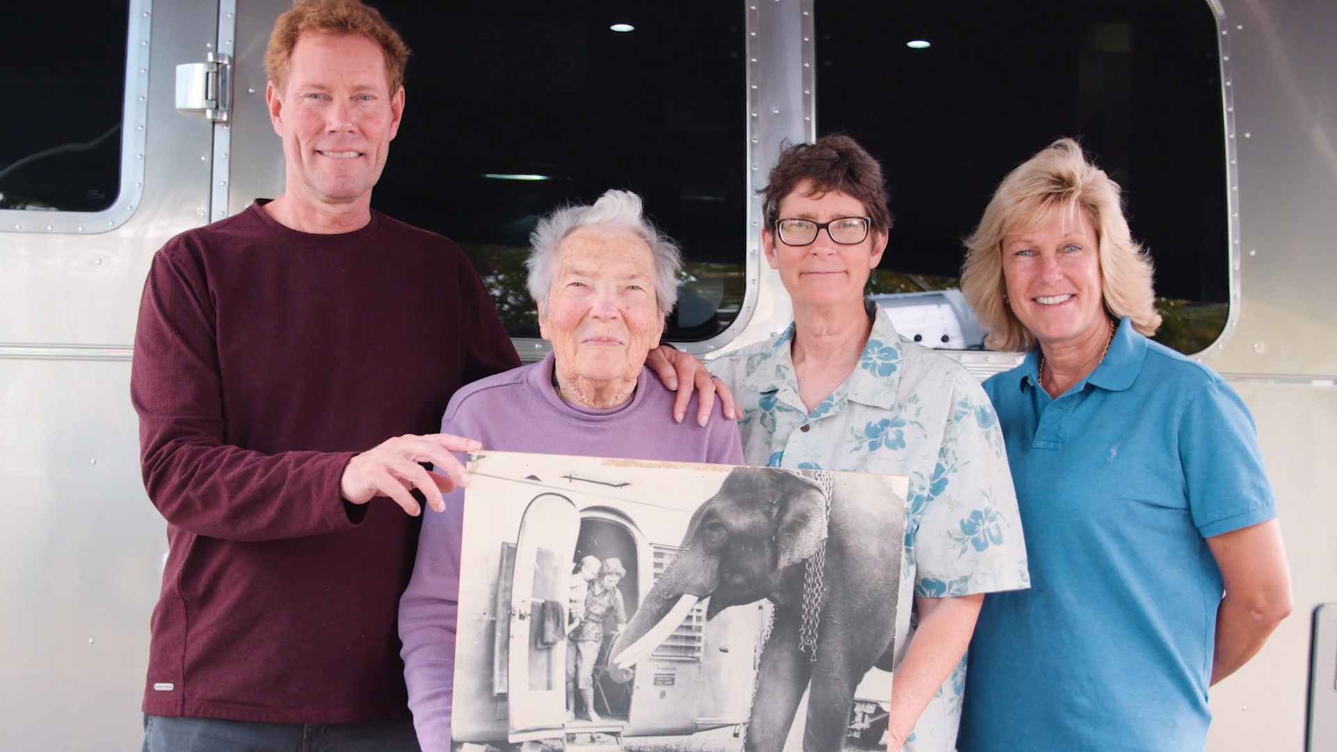 The Smith family in front of an Airstream Travel Trailer holding up an image from the Airstream Around the World Caravan