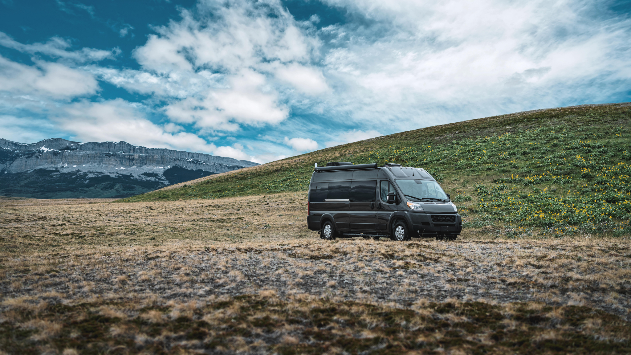 Airstream Rangeline Class B Motorhome with black exterior and built on a RAM chassis is parked in a field with mountains in the background.