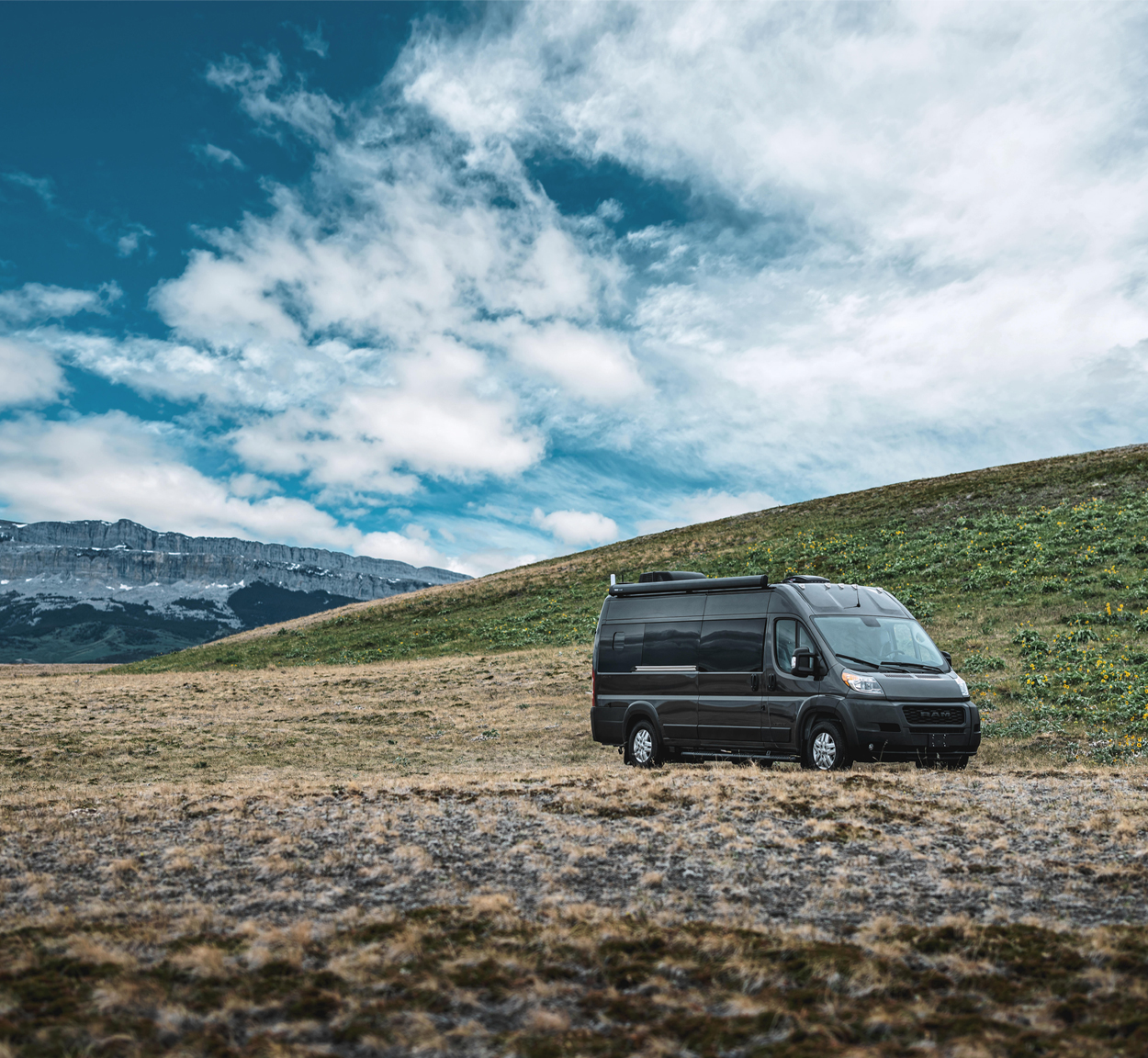 Airstream Rangeline Class B Motorhome with black exterior and built on a RAM chassis is parked in a field with mountains in the background.