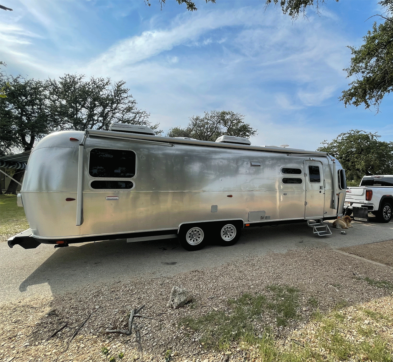 An Airstream International Travel Trailer camper being towed by a white truck down the road.