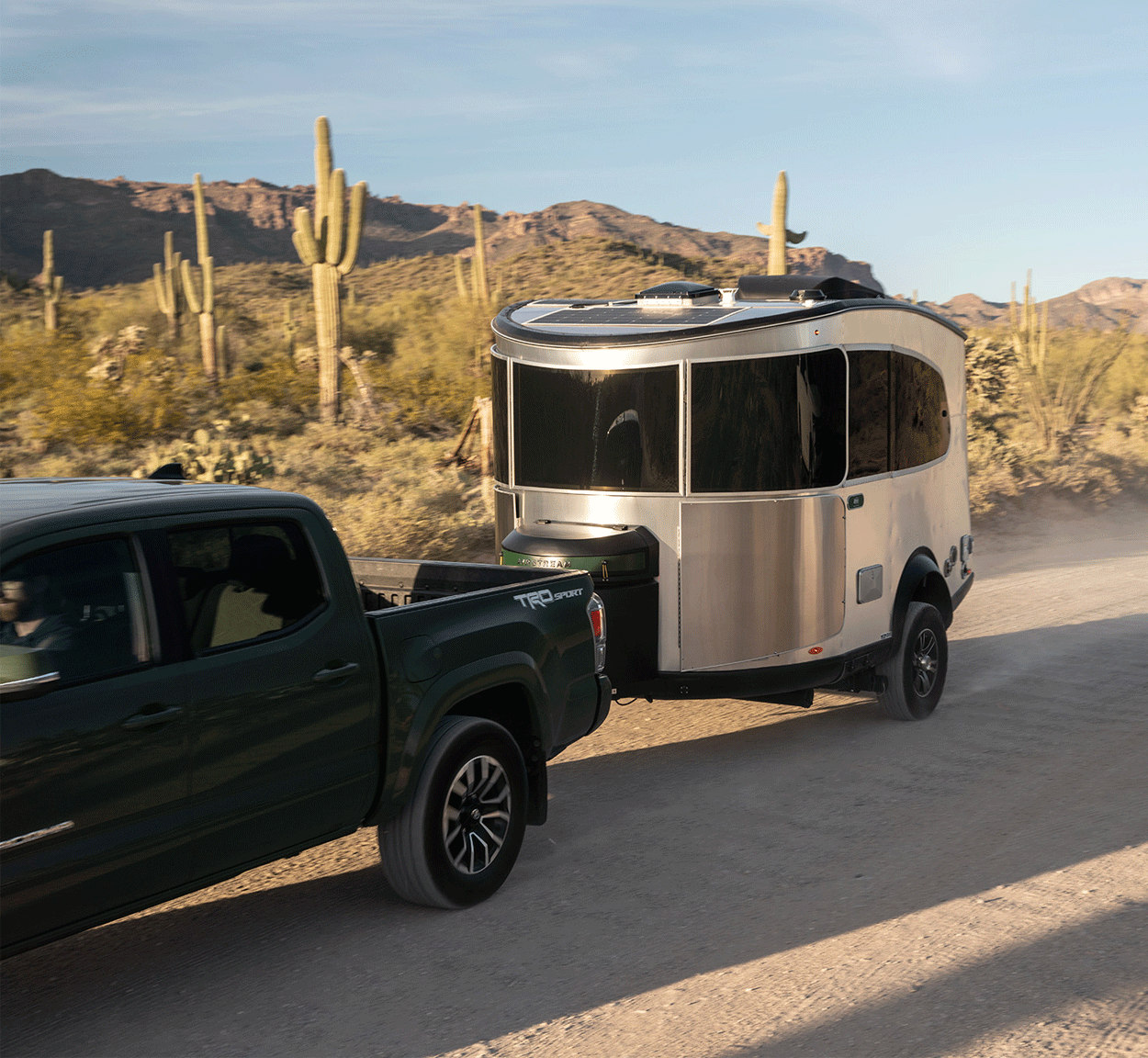 The Airstream REI Co-op Special Edition Travel Trailer being towed by a green truck down a dirt road in Sedona, Arizona.