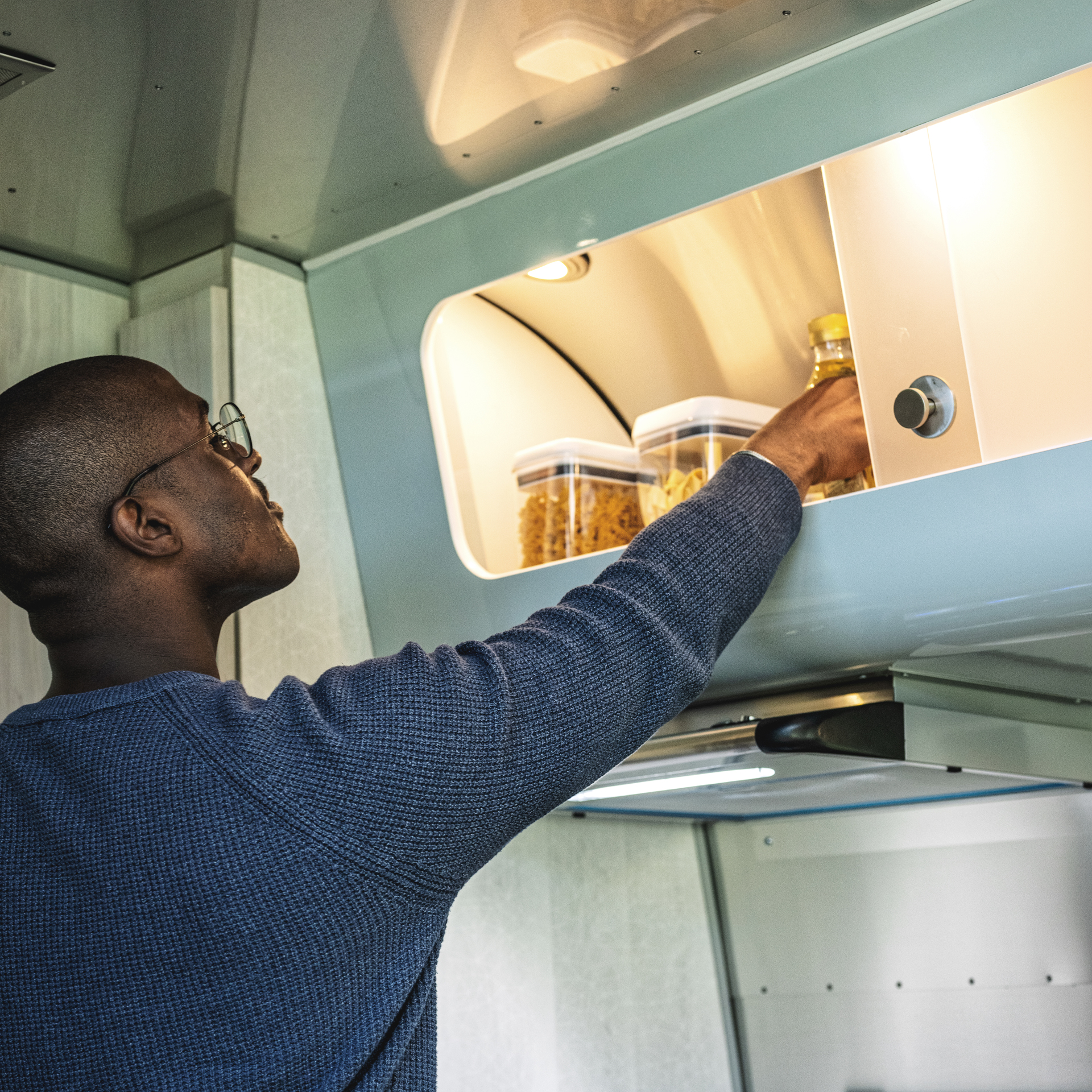 A man putting food away in the storage about the stove in the Airstream International travel trailer.