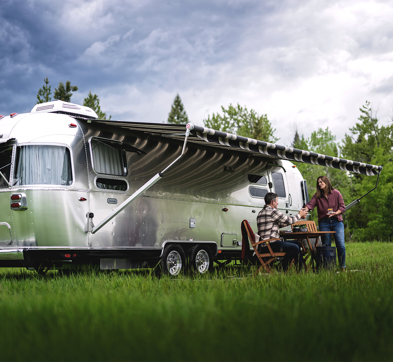 A couple outside under the awning of their Airstream Globetrotter travel trailer while they sit at a table.