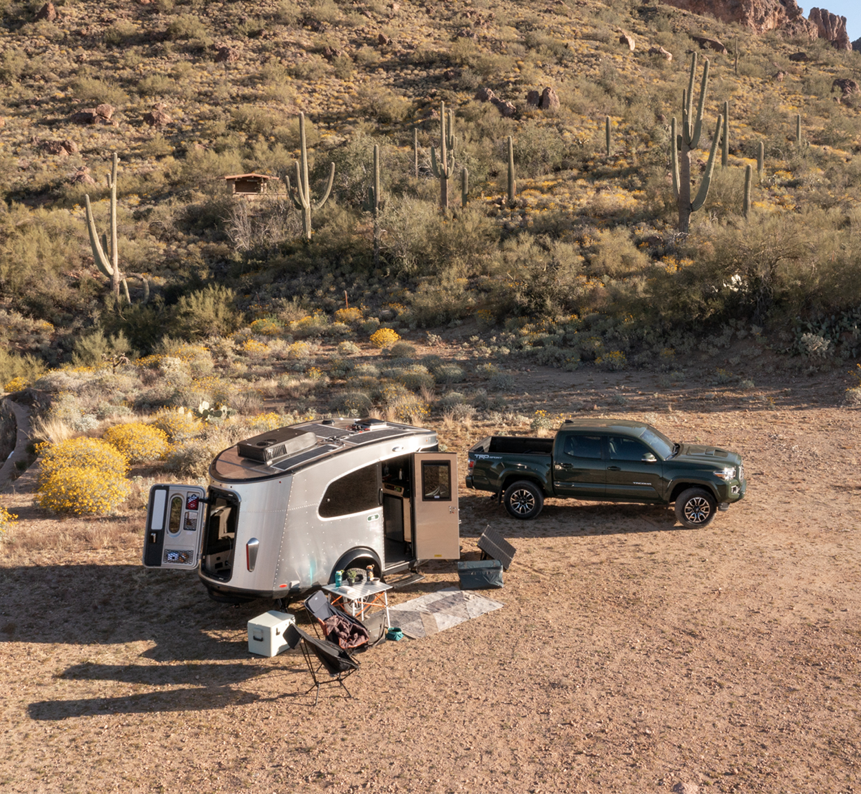An Airstream REI Co-op Basecamp travel trailer parked at a spot in Arizona with the campsite set up and a green truck parked next to the camper.
