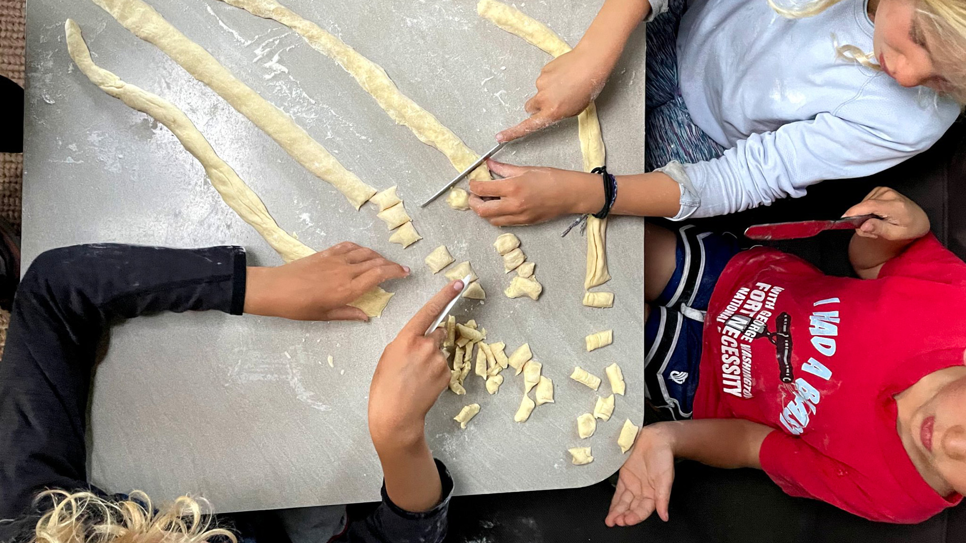 Three campers sitting at a table in their Airstream travel trailer making pasta.