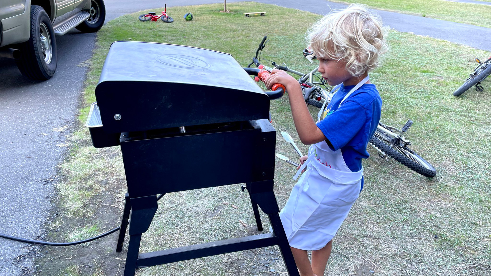 A boy camper grilling in the evening while his family camps in their Airstream travel trailer.