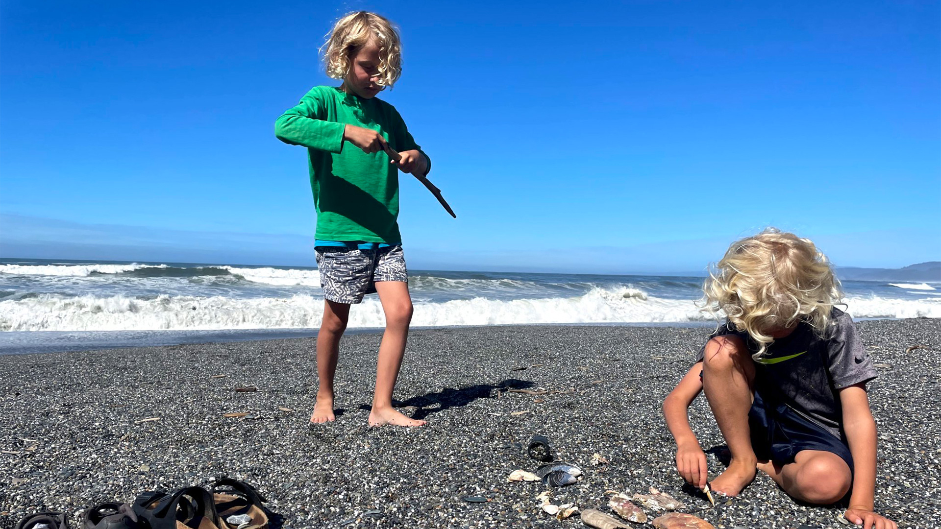 Two kids playing in the sand with sticks next to a body of water.
