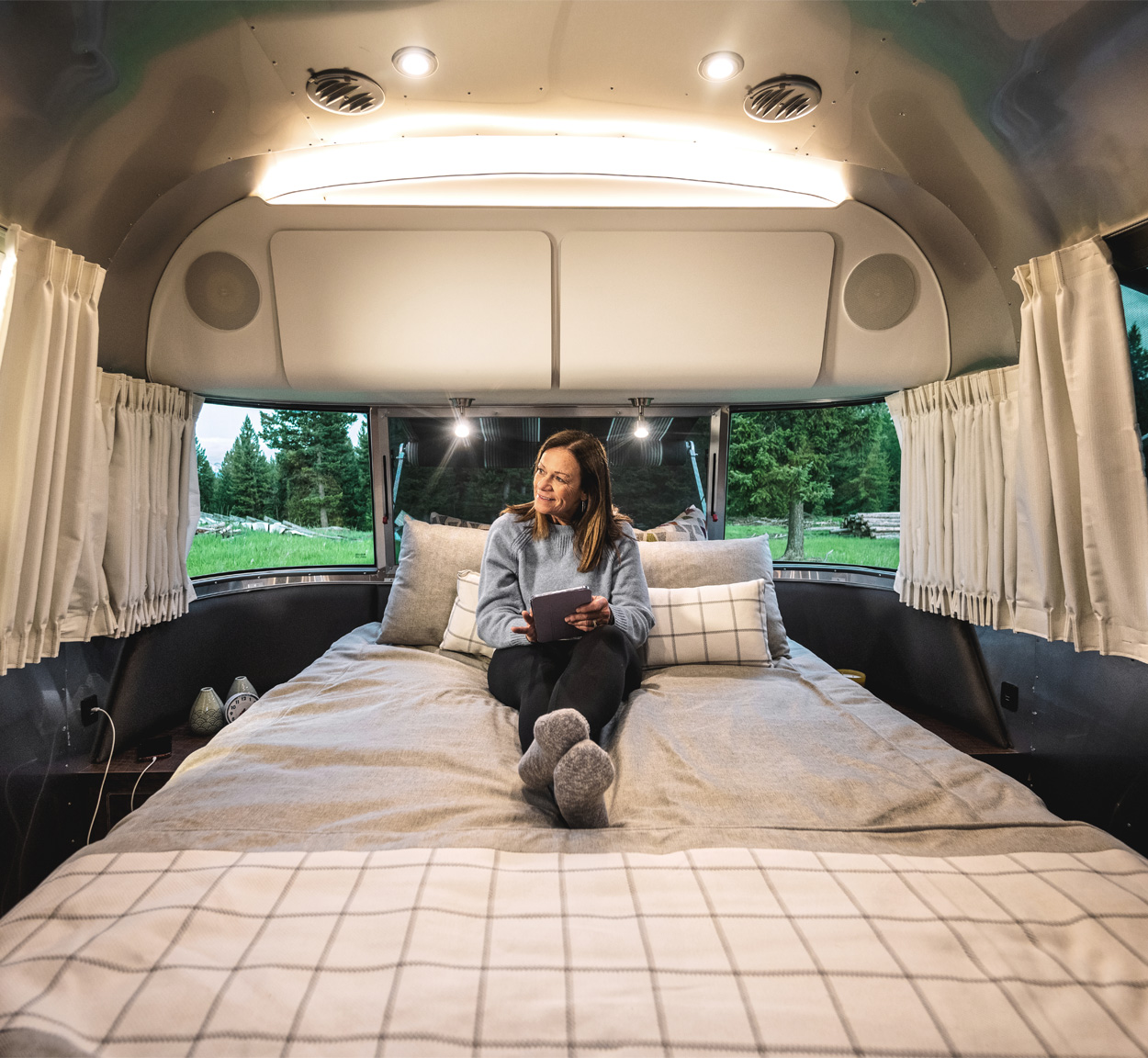 A woman camper sitting on the bed looking at her tablet in her Airstream Globetrotter travel trailer.
