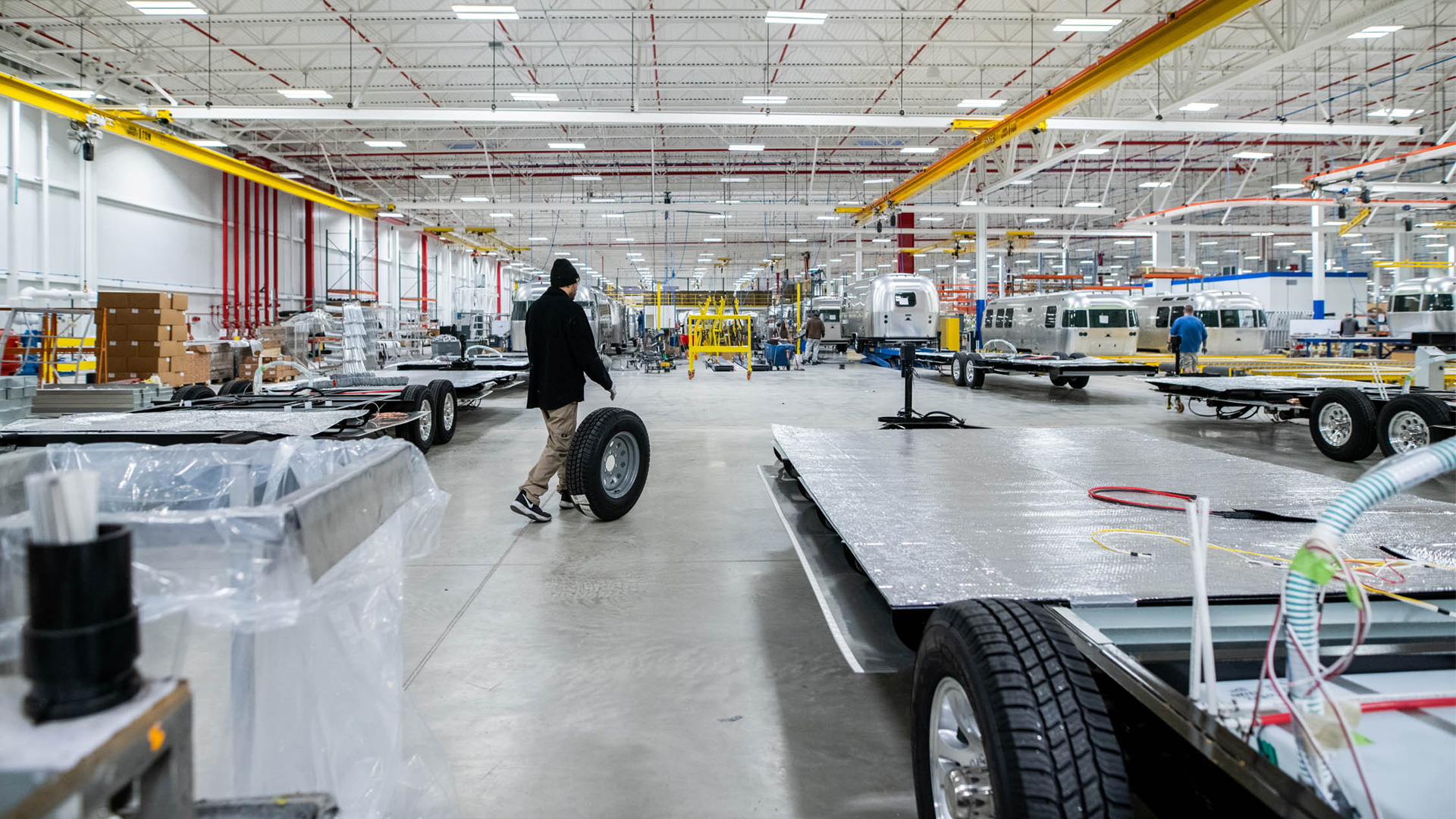 A man wheeling a wheel over to an Airstream travel trailer chassis while building the travel trailer.
