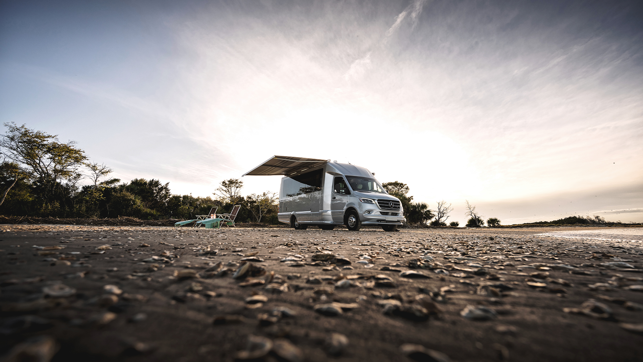 An Airstream Atlas Touring Coach parked on a beach and campers have out the awning.
