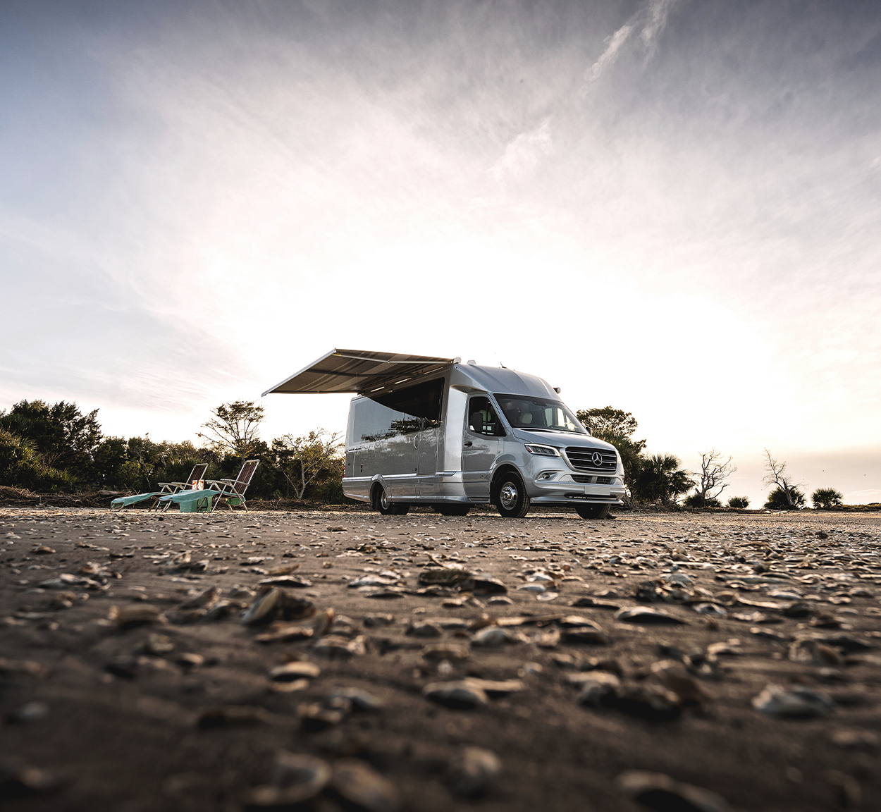 An Airstream Atlas Touring Coach parked on a beach and campers have out the awning.