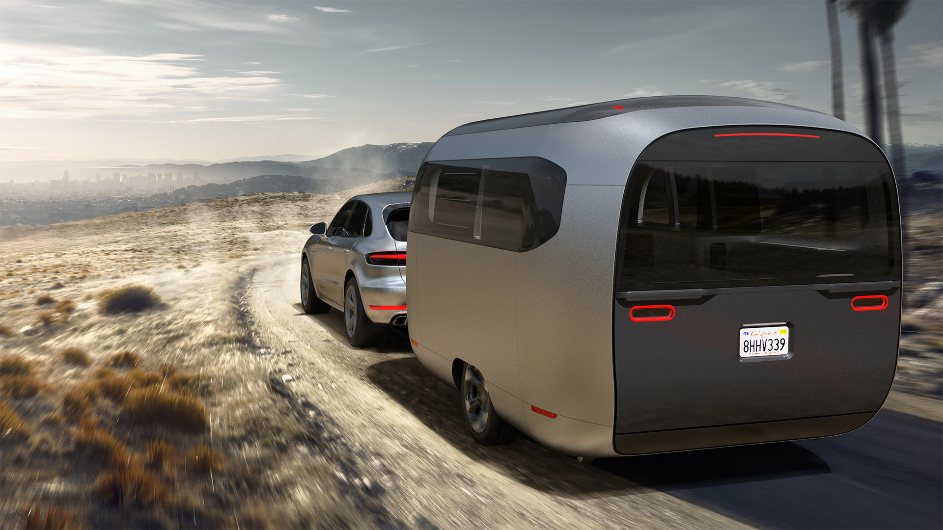 Airstream Studio F. A. Porsche Concept Travel Trailer being towed down a gravel road by a Porsche vehicle.