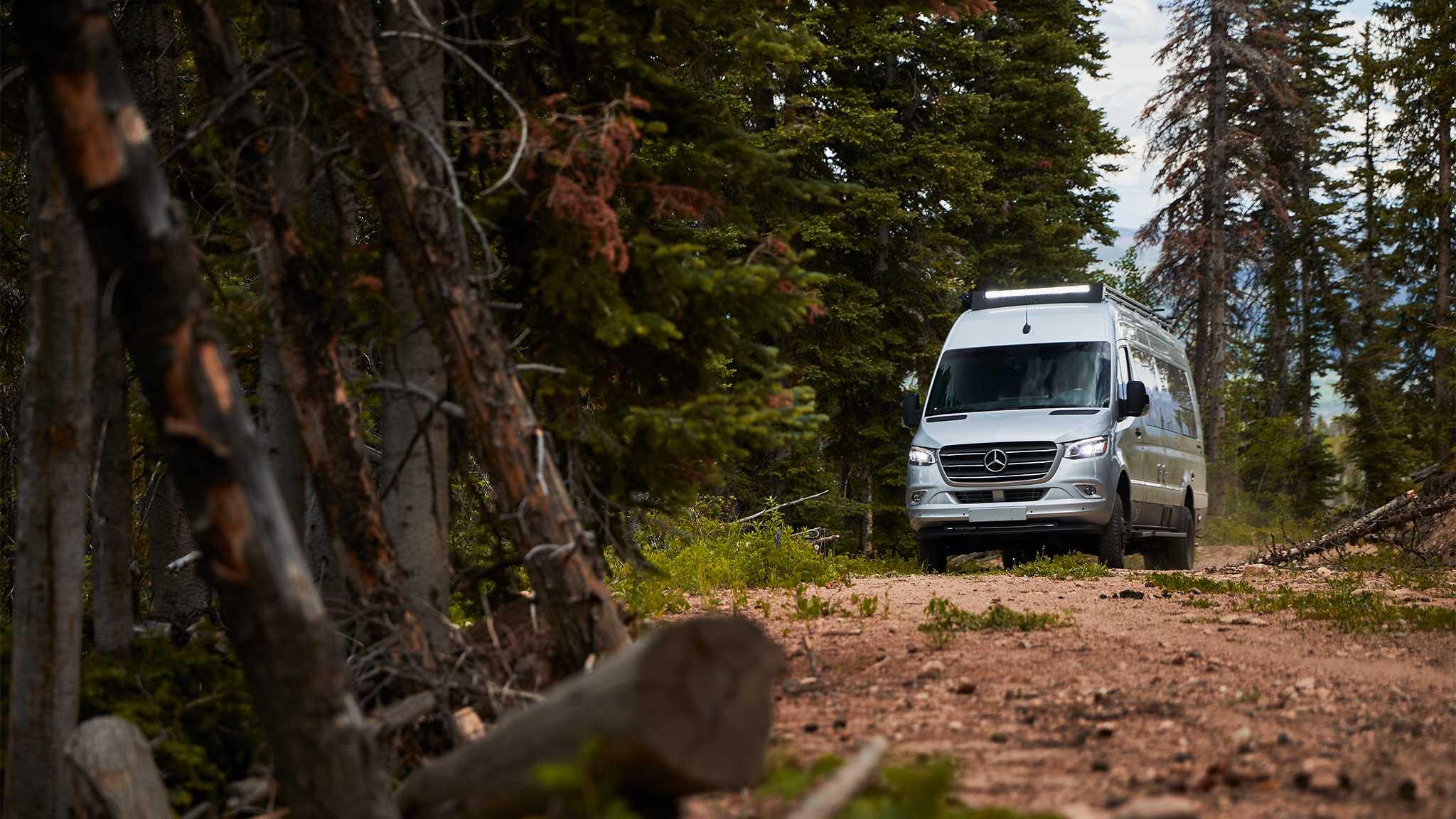 An Airstream 24X Class B Motorhome off the road driving down a dirt path through a forest.