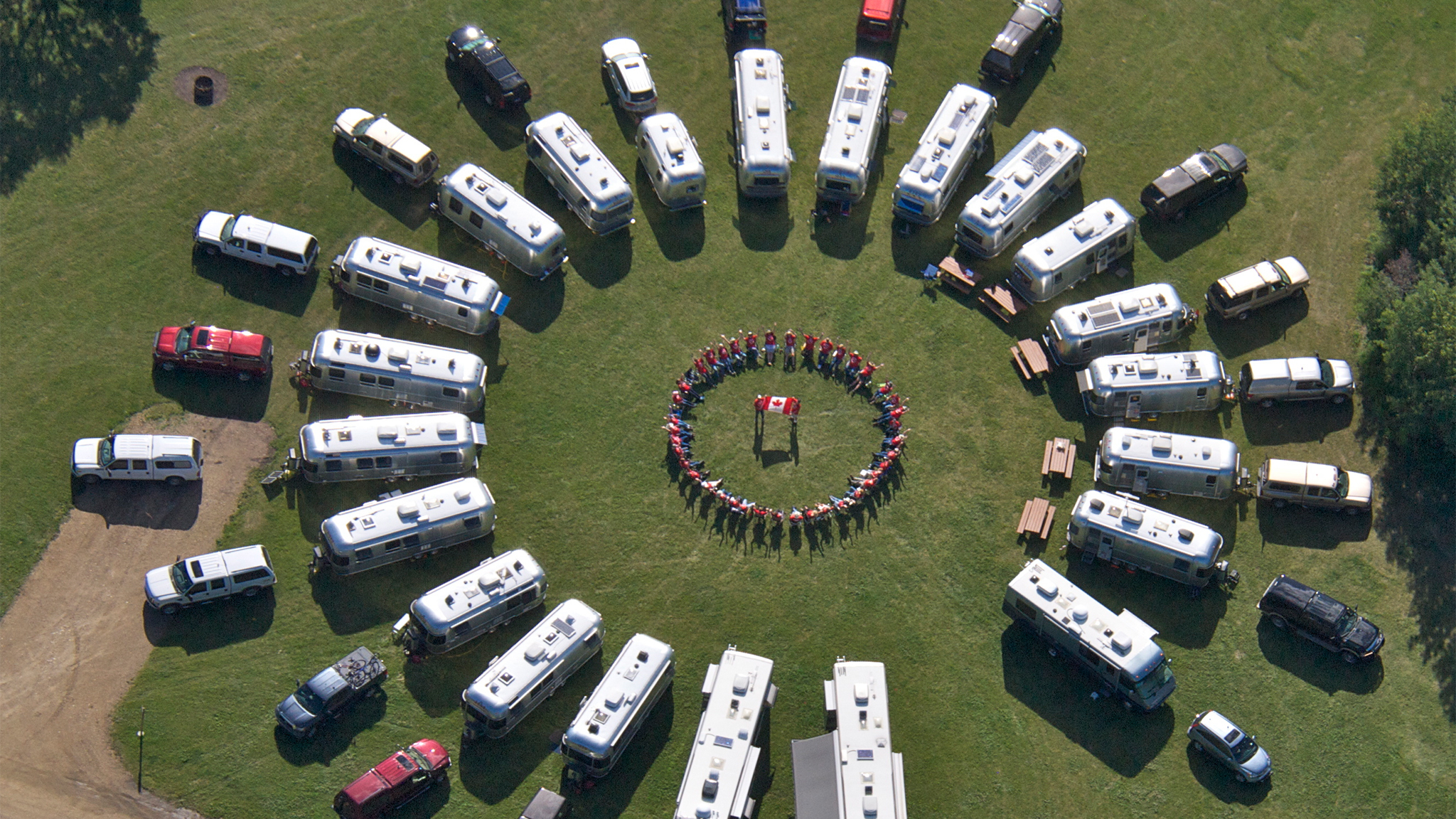 Airstream travel trailers lined up in a circle with campers standing in the middle holding a flag.