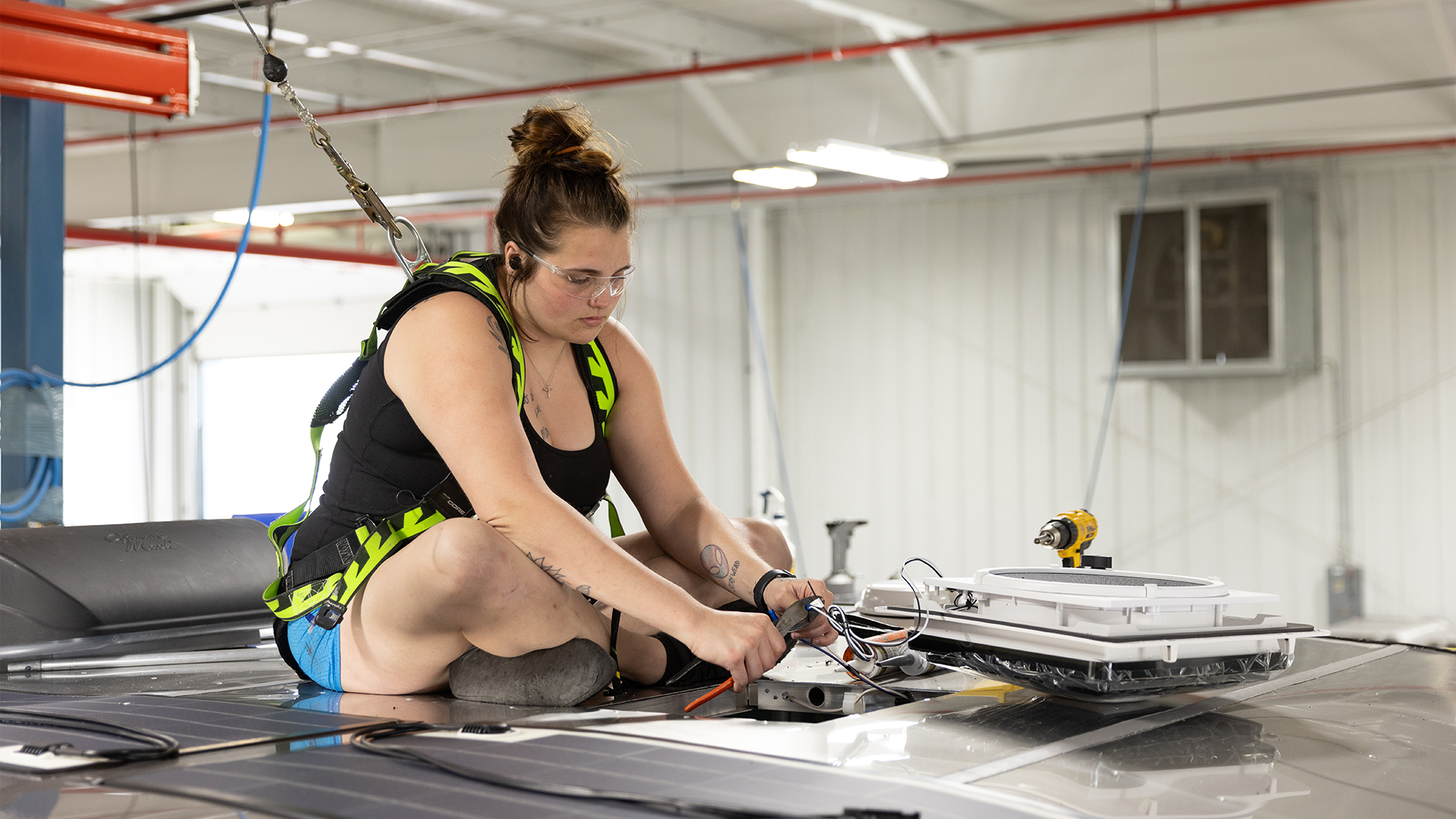An Airstream employee installing an air conditioner and solar panels on the roof of an Airstream Basecamp travel trailer