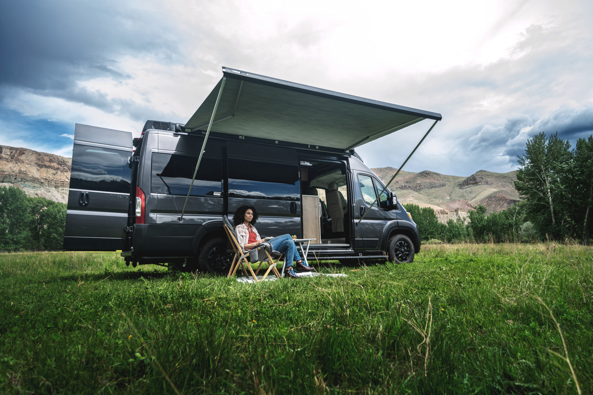 A woman sitting under the awning of her Airstream Rangeline Touring Coach