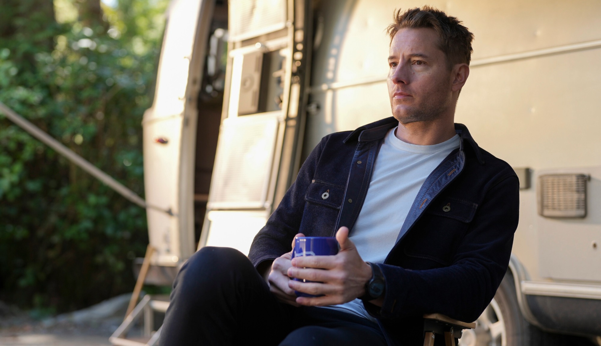 Justin Hartley sitting outside of Airstream travel trailer that is featured in the show 'Tracker'