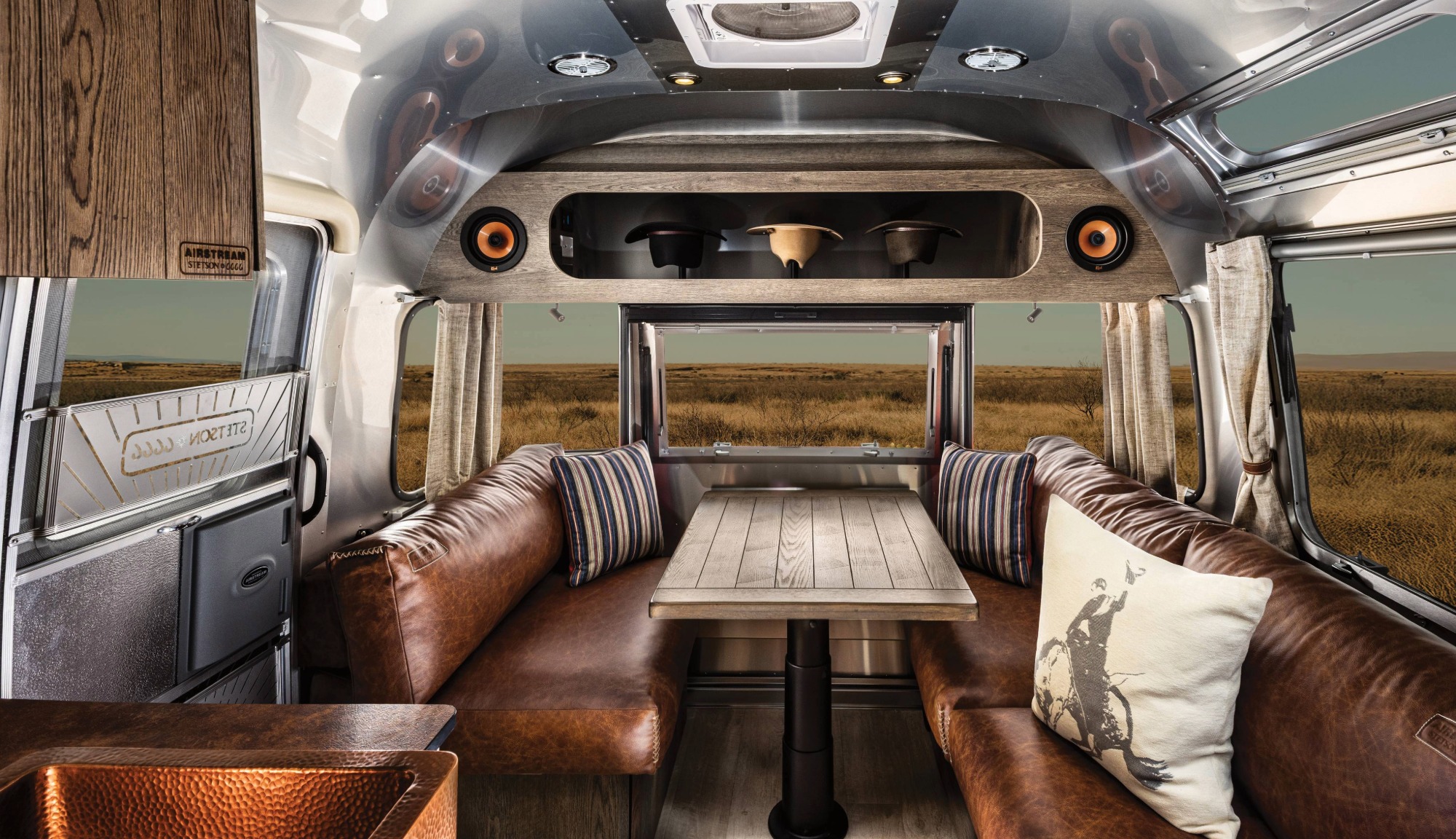 Interior studion image of the Airstream Stetson + 6666s Limited Edition Travel Trailer featuring the hat rack, leather couch, oakwood dinnette, and copper sink.