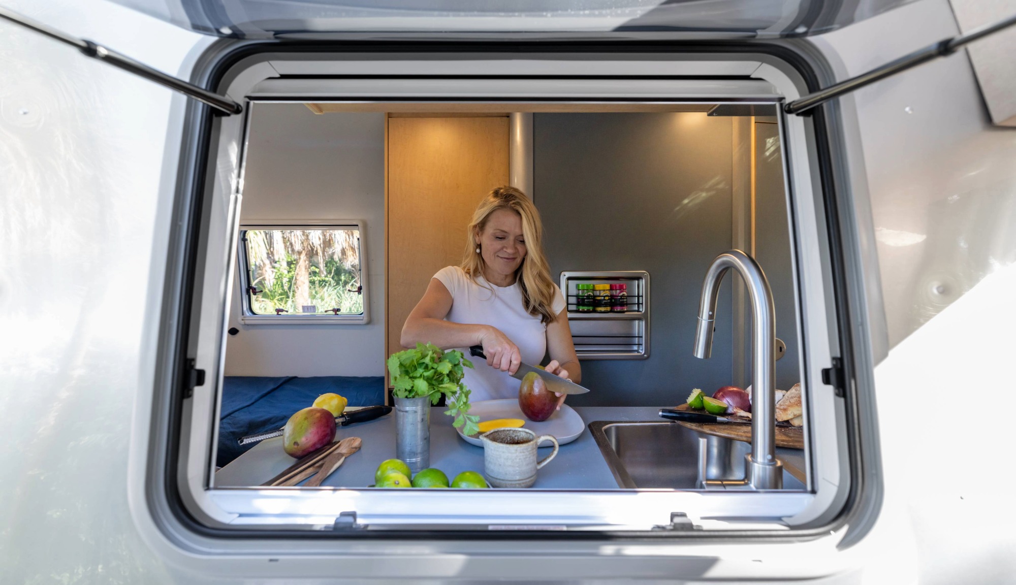 Looking through exterior window at Tricia Leach cooking in Airstream World Traveler