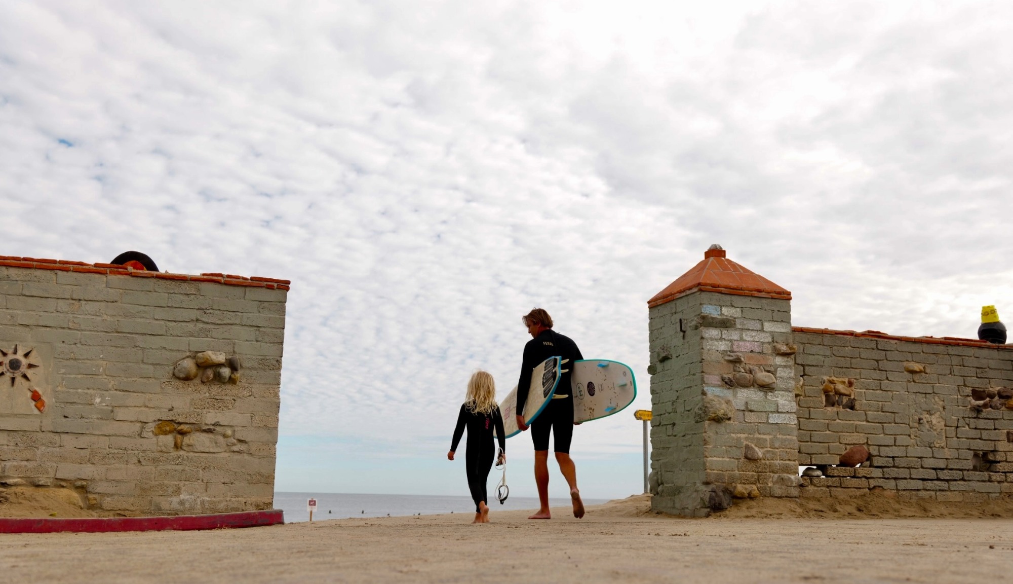 Damien Fahrenfort and his daughter walking to the ocean holding their surfboards