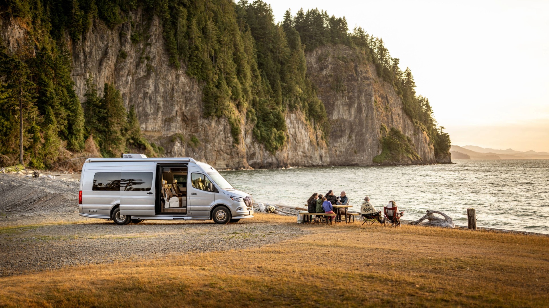 Airstream Interstate 24GL Boondocking on a coast and a family eating at a picnic table beside it 