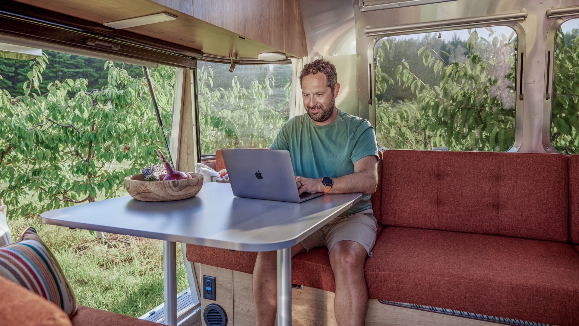 Man working on laptop sitting at the dinette in an Airstream Trade Wind