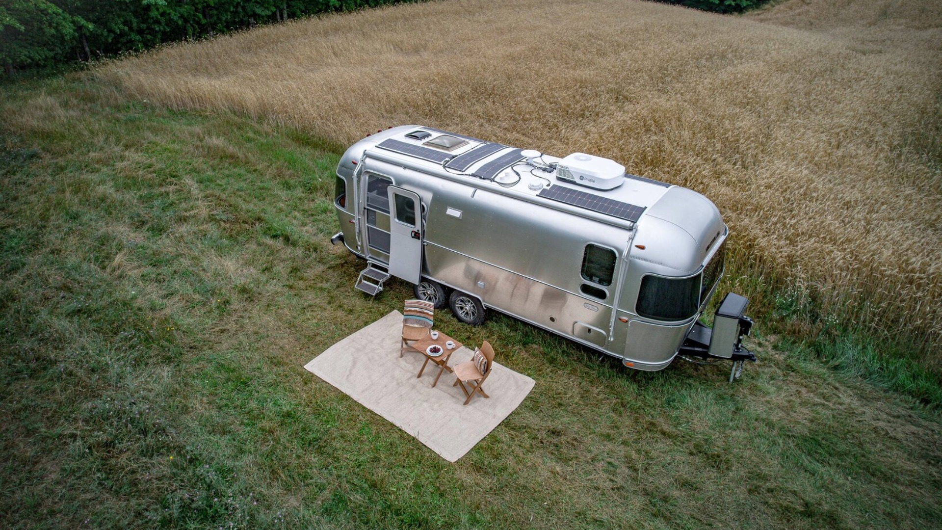 Birdeye view of Trade Wind travel trailer boondocking in a field with camping chairs set up, featuring the solar panels on top