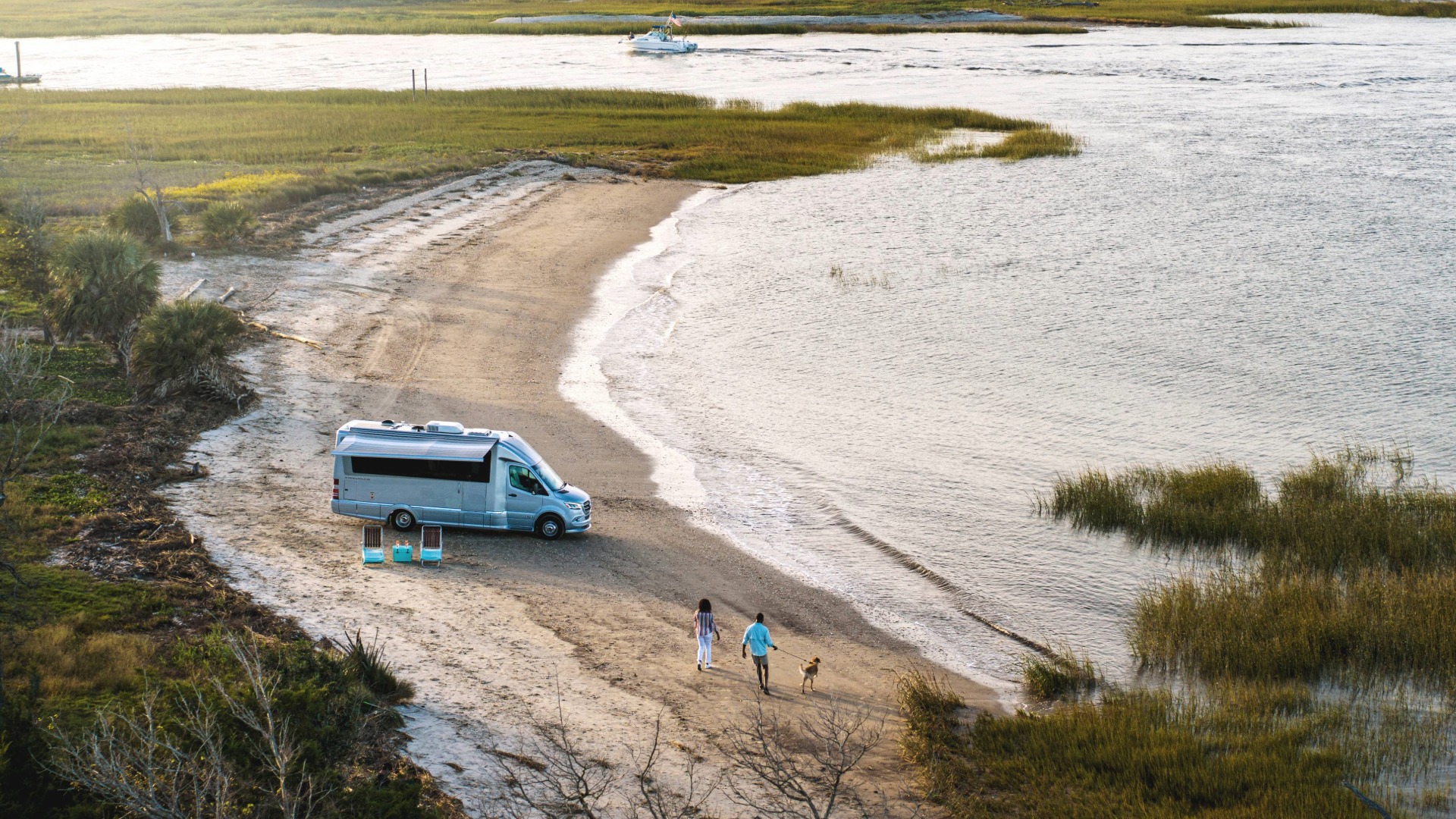 Couple walking their dog on a beach in front of an Airstream Atlas Camper Van