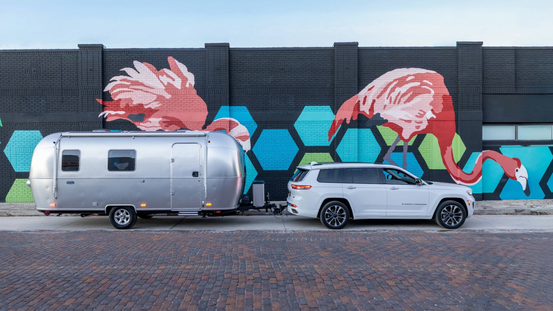Jeep Grand Cherokee towing the Airstream World Traveler Travel Trailer in front of a flamingo mural