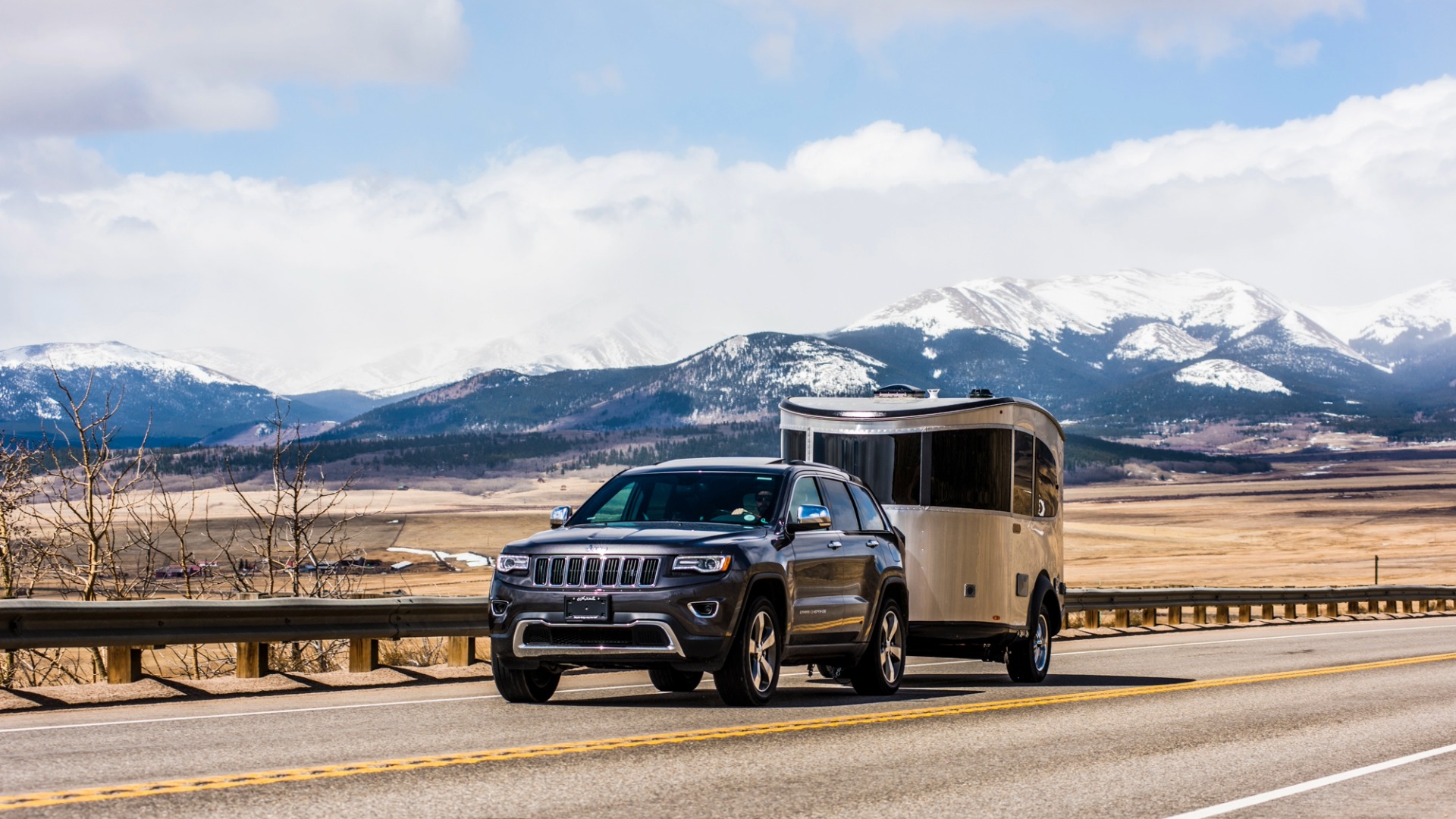 Airstream Basecamp being towed by a blue Jeep Grande Cherokee in the mountains