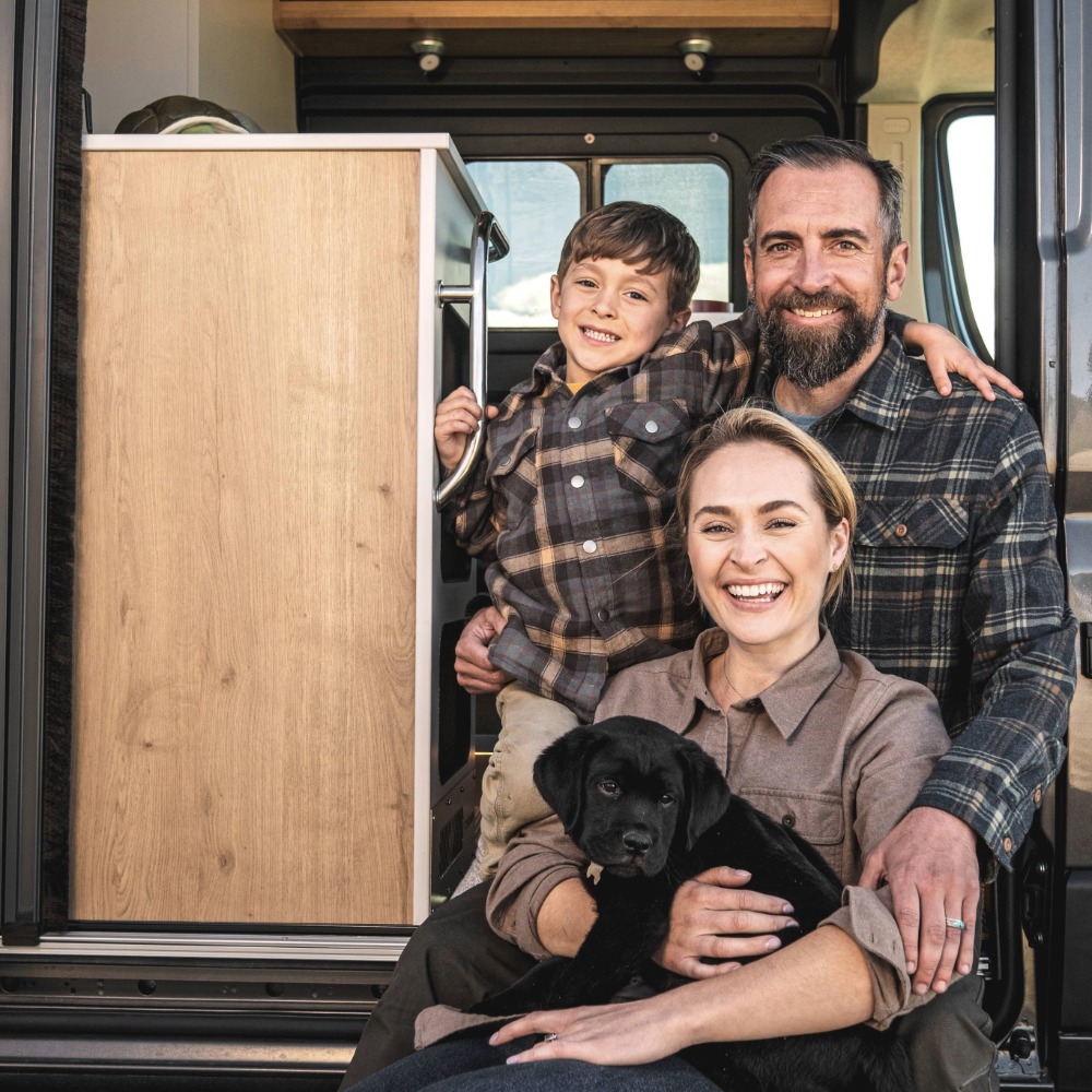 Family and puppy sitting on the steps of the Rangeline Camper Van