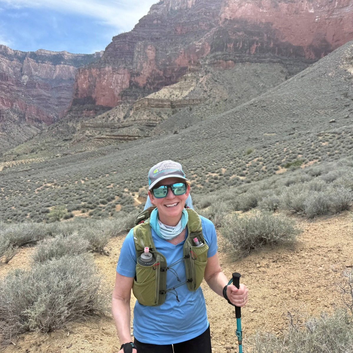 Woman smiling and posing in front of a mountain with hiking equipment