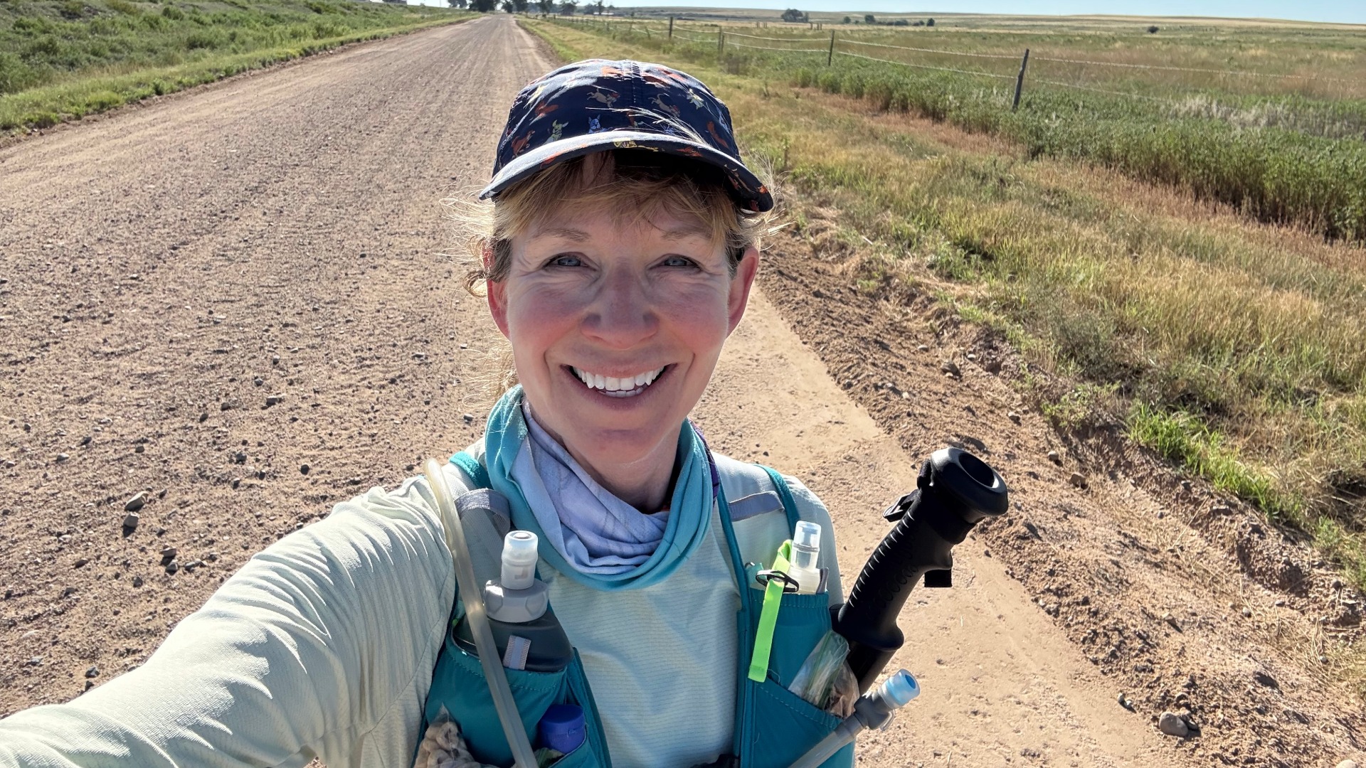 Woman in hat taking a selfie in running gear, posed in front of a dirt road