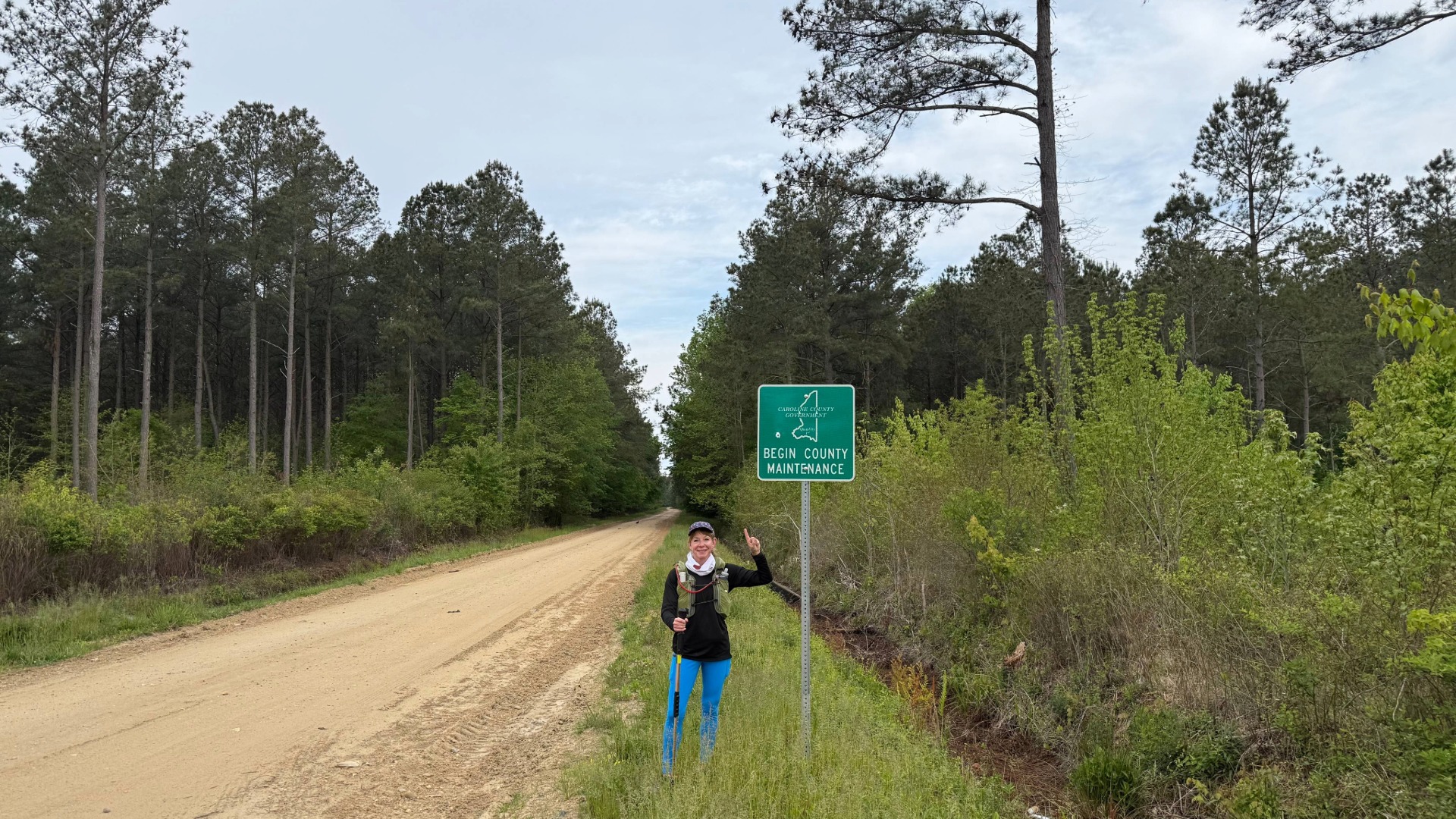 woman in running gear pointing to a trail sign on a rural running trail
